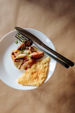 Küçük porsiyon incir ve jambonlu aperatif beyaz tabakta kraker ve çatal bıçak. Rustik el işi kağıt arka planı.