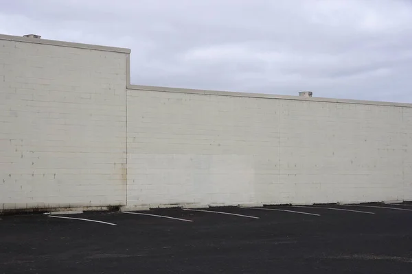 White painted warehouse back cement brick wall under cloudy sky bordering a parking lot
