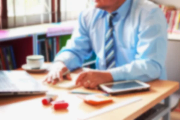 blurred office background , office worker at hand working with digital tablet and laptop and notebook on wooden desk in office