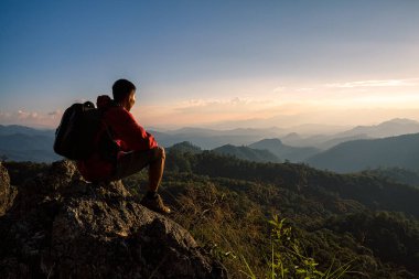 Sırt çantalı genç turist kayalıklarda dinleniyor ve günbatımının tadını çıkarıyor.