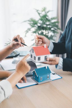 Hesap makineli küçük ev modelini müşteriye gösteren emlakçıya yakın çekim, masa başında kontrat belgeleri, ipotek kredisi konsepti, ev sahipliği, emlak yatırım anlaşması. mortgage kredisi