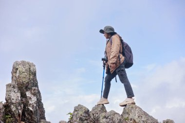 Yürüyüş direğiyle kayalık kayalıklarda duran yürüyüşçü, macera, güven, meydan okuma, keşif, açık hava yaşam tarzı, başarı ve dağ doğasında seyahat ilhamının sembolü..