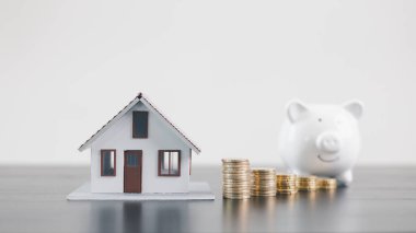 Bozuk paralar ve beyaz kumbaralı mini ev modeli, mortgage kredisi, emlak yatırımı, emlak finansmanı, tasarrufu, sigortası, refah yönetimi ve konut ekonomisi kavramını temsil eden.