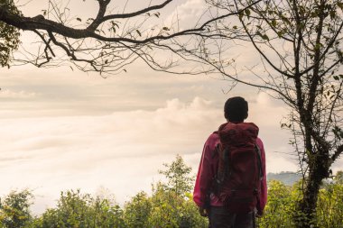 Sırt çantalı gezgin dağın tepesinde durup sislerin, macera yaşam tarzı konseptinin, yürüyüşün, özgürlüğün, keşfin ve açık hava seyahatinin ilham kaynağının üzerinde manzaralı gündoğumuna bakıyor..
