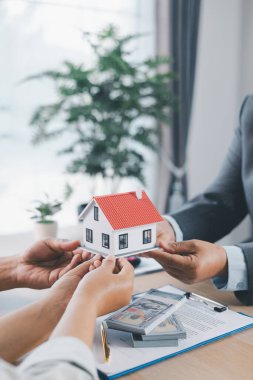 Emlak acentesinin hesap makinesi ve kontrat evraklarıyla müşteriye ev modelini teslim etmesi, ipotek kredisi konsepti, ev sahipliği, emlak yatırımı ve konut anlaşması.