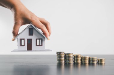Üst üste dizilmiş madeni paraların üzerindeki el ele tutuşan ev modeli, mortgage kredisini, emlak yatırımını, emlak finansmanını, tasarrufları, zenginlik büyümesini, ev sahipliği ve konut ekonomisini simgeliyor..