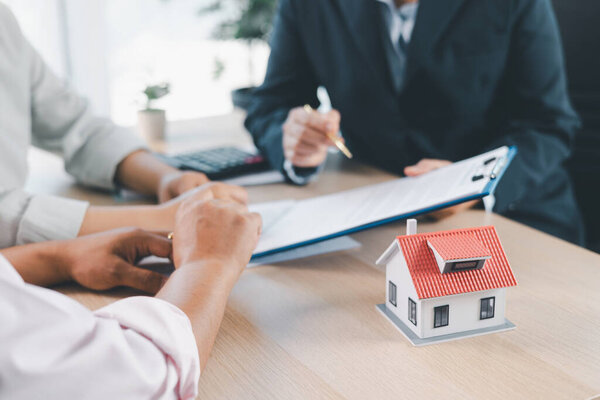 House model on desk with blurred people discussing contract in background, concept of real estate investment, mortgage loan, home ownership, property business and financial agreement.