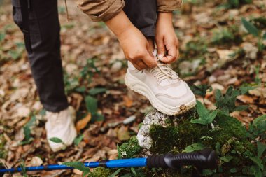 Yürüyüşçülerin ayakkabı bağcıklarını ormanda yürüyüş direğiyle bağlamaları, hazırlık, macera, açık hava yaşam tarzı, yürüyüş, yolculuk ve doğa yolunda keşif sembolleri. macera yürüyüşü