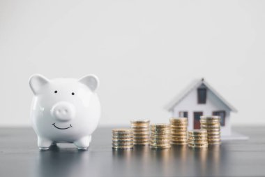 Bozuk paralar ve beyaz kumbaralı mini ev modeli, mortgage kredisi, emlak yatırımı, emlak finansmanı, tasarrufu, sigortası, refah yönetimi ve konut ekonomisi kavramını temsil eden.