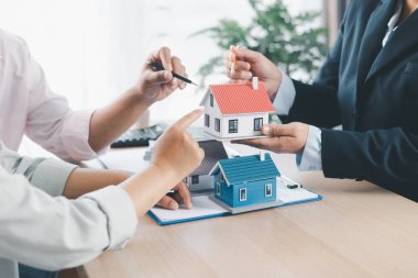 Hesap makineli küçük ev modelini müşteriye gösteren emlakçıya yakın çekim, masa başında kontrat belgeleri, ipotek kredisi konsepti, ev sahipliği, emlak yatırım anlaşması. mortgage kredisi