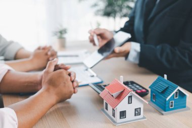 Ev modeli, arka planda sözleşme, emlak yatırımı konsepti, ipotek kredisi, ev sahipliği, gayrimenkul ticareti ve mali anlaşma konularını tartışan bulanık insanlarla birlikte masada..