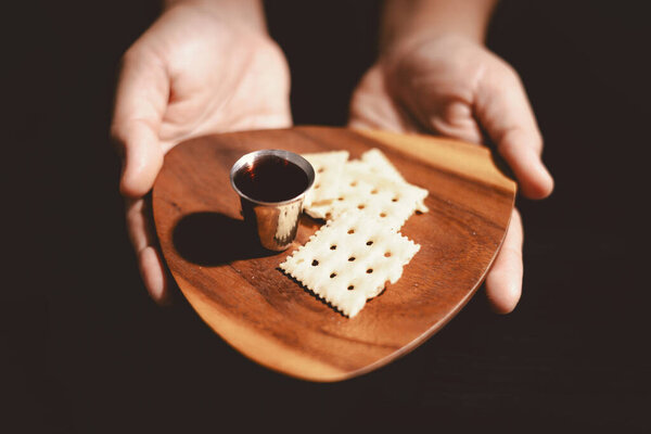 Руки, держащие хлеб причастия с деревянной чашей и чашей вина, символизирующие Святое Причастие, Евхаристию, жертву Иисуса Христа и христианскую веру в Вечерю Господню.