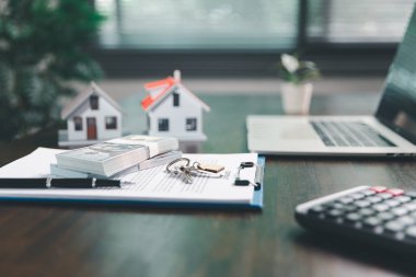 Masanın yanına yerleştirilen ev modeli madeni paraların yanı sıra, evrak işleri de gayrimenkul yatırımını, emlak değerini, mali planlama, mortgage seçeneklerini, emlak piyasasındaki pazar analizini simgeler..