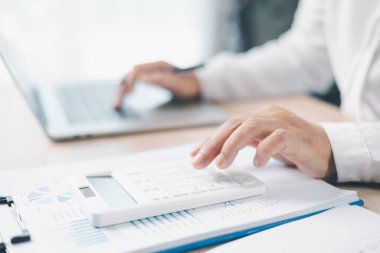 Finansal planlama ve muhasebe kavramı. Bir iş kadını raporları ve çizelgeleri analiz etmek, bütçe ve yatırım stratejisini ofis masasında odaklanma ve hassasiyetle hesaplamak için hesap makinesi kullanır..