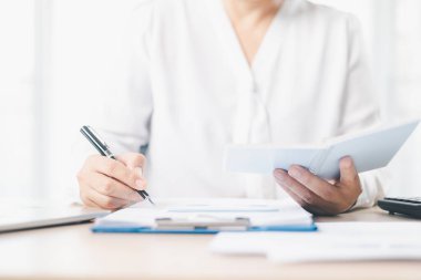 Bir iş kadını, elinde belgelerle birlikte defter tutarken panoya notlar yazar. İş planlama, muhasebe, mali yönetim, üretkenlik ve kurumsal strateji kavramı.