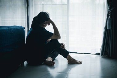 Yalnız bir kadın karanlık odada elleri başının üstünde pencere kenarında oturur. Depresyon, üzüntü, endişe, stres, zihinsel sağlık sorunu, yalnızlık ve duygusal mücadele kavramı.