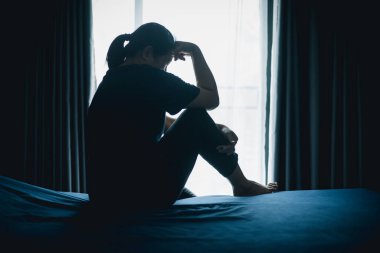 Stresli bir kadın karanlık bir odada tek başına oturuyor, başını eğiyor, depresyonu, endişeyi, umutsuzluğu, yalnızlığı, zihinsel sağlık mücadelesini, tükenmiş ve duygusal acıyı simgeliyor..