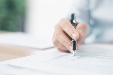 Vergi beyannamesi ve mali belgeler. İş kadınlarının ellerinin kalem tutması ve vergi formuna işaret etmesi, muhasebe, yasal evraklar, bütçe planlaması ve finansal doğruluğu simgeliyor.