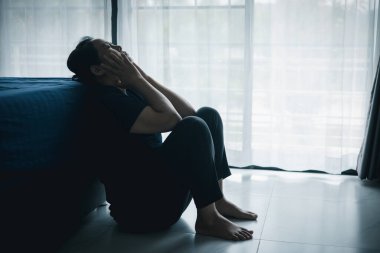 Yalnız bir kadın karanlık odada elleri başının üstünde pencere kenarında oturur. Depresyon, üzüntü, endişe, stres, zihinsel sağlık sorunu, yalnızlık ve duygusal mücadele kavramı.