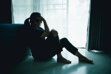 Yalnız bir kadın karanlık odada elleri başının üstünde pencere kenarında oturur. Depresyon, üzüntü, endişe, stres, zihinsel sağlık sorunu, yalnızlık ve duygusal mücadele kavramı.