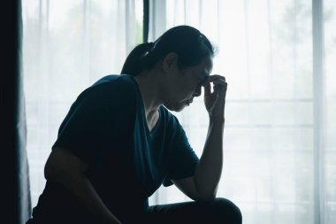 Stresli bir kadın karanlık bir odada tek başına oturuyor, başını eğiyor, depresyonu, endişeyi, umutsuzluğu, yalnızlığı, zihinsel sağlık mücadelesini, tükenmiş ve duygusal acıyı simgeliyor..