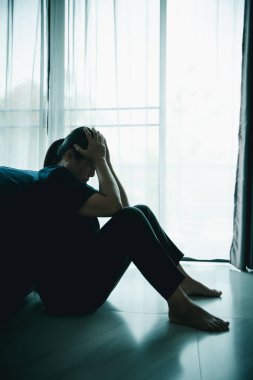 Yalnız bir kadın karanlık odada elleri başının üstünde pencere kenarında oturur. Depresyon, üzüntü, endişe, stres, zihinsel sağlık sorunu, yalnızlık ve duygusal mücadele kavramı.