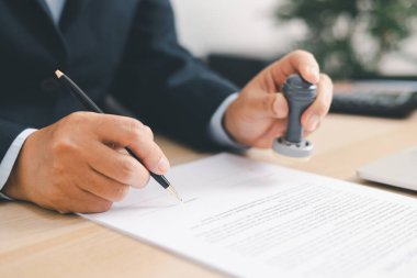 İşadamı resmi belgeleri masasında imzalayıp damgalıyor, yasal sözleşme onayı, yetki belgesi ya da iş anlaşmasının kurumsal arka planda onaylanması. pul onayı