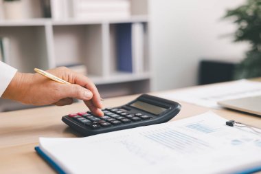 Ofis masasında mali raporlu hesap makinesi ve dizüstü bilgisayar kullanan işadamları, muhasebe analizi, bütçe planlaması, veri yönetimi ve kurumsal finans stratejisi kavramı.