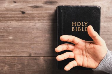 Kutsal İncil 'in üzerinde dua eden eller ahşap masada, Hristiyan inancını, ibadeti, bağlılığı, Tanrı' ya olan güveni kilise, dua ve meditasyon kavramlarını simgeliyor..