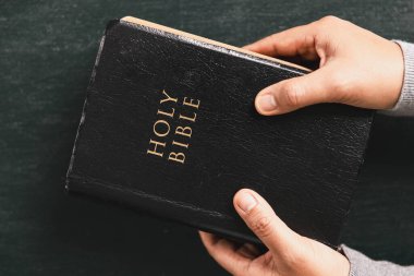 Kutsal İncil 'in üzerinde dua eden eller ahşap masada, Hristiyan inancını, ibadeti, bağlılığı, Tanrı' ya olan güveni kilise, dua ve meditasyon kavramlarını simgeliyor..