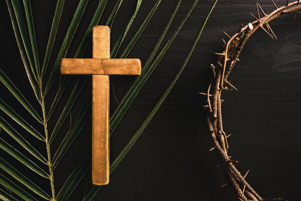 Wooden cross placed on green palm leaves with crown of thorns, symbolizing Christian faith, Palm Sunday, sacrifice, Easter reflection, religious concept for worship, prayer, church design.