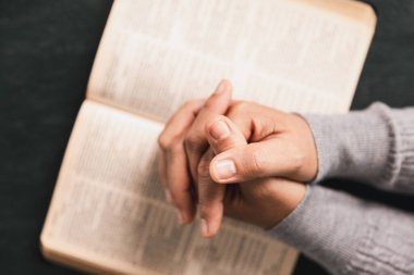 Kutsal İncil 'in üzerinde dua eden eller ahşap masada, Hristiyan inancını, ibadeti, bağlılığı, Tanrı' ya olan güveni kilise, dua ve meditasyon kavramlarını simgeliyor..