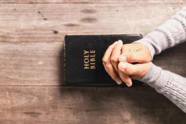 Kutsal İncil 'in üzerinde dua eden eller ahşap masada, Hristiyan inancını, ibadeti, bağlılığı, Tanrı' ya olan güveni kilise, dua ve meditasyon kavramlarını simgeliyor..