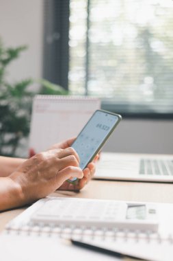 Ofis çalışanı masadaki mali numaraları hesaplamak için akıllı telefon hesap makinesi kullanıyor, dijital muhasebe, bütçe izleme, masraf izleme, modern iş akışı ve profesyonel mali yönetim örneklerini gösteriyor.