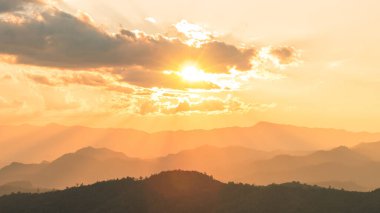 Katmanlı dağ siluetleri üzerinde parlak gün doğumu dramatik bulutlar altında, güneş ışınları ve sisli sıcak altın gökyüzü, seyahat, motivasyon, doğa damgası için fotokopi alanı ile manzara arka planı.