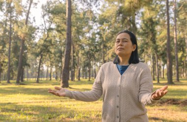 Avuç içi açık bir kadın huzurlu bir çam ormanında dua ediyor. Gözler zihin meditasyonu için kapalı. Doğada ruhani ibadet ve minnettarlık, fotokopi alanı ile sakin ve sağlıklı bir zemin..