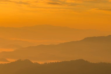 Sıcak turuncu gündoğumu katmanlı dağ sırtlarını ve şafak vakti sisli vadileri, yukardaki yumuşak bulutları boyar. Kopya alanı, sakin atmosfer, seyahat ve doğa kavramına sahip en küçük manzara arkaplanı.