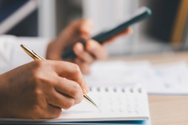 Akıllı telefon tutarken, görevleri düzenlerken, iş verimliliği, planlama ve uzaktan iş iletişimi harcamaları için bütçe belirlerken ve izleme yaparken ellerin yakın plan defterine notlar yazması.