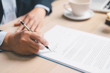 Takım elbiseli avukat, arka planda adalet terazileri, yasal hizmetleri temsil eden, uyum gözden geçirme, anlaşma onayı ve belgelerle birlikte ofis masasında bir sözleşme imzaladı..