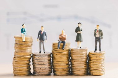 Madeni para yığınları üzerinde çalışan minyatür işadamları, bulanık mali rapor geçmişi, gelir eşitsizliğini, maaş hiyerarşisini, zenginlik dağılımını ve yatırım büyüme kavramını sembolize ediyor.