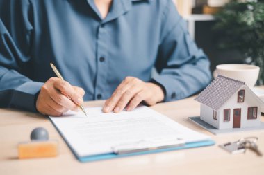 Panoda ev modeli ve anahtarlarının yanında emlak sözleşmesi imzalayan, ev satın alma, ipotek veya kira sözleşmesi, emlak sigortası ve ofis masasında kredi onayı imzalayan kişi.