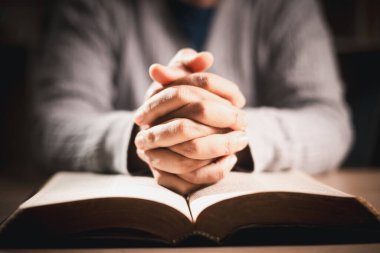 Açık bir kitap, sıcak bir ışık ve sığ bir alan derinliği üzerinde dua ederken, evde sessiz bir çalışma sırasında inanç, bağlılık, yansıma ve ruhsal rehberlik umudunu sembolize eder..