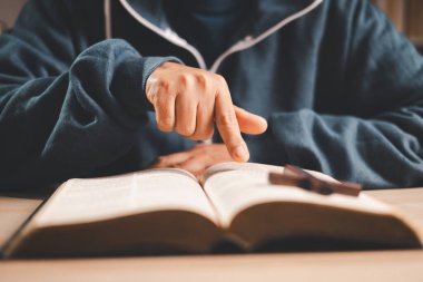 Masada açık bir İncil okuyan bir adam, sığ bir alan derinliği ile sayfaları sıcak kapalı ışık altında çevirmek, Hıristiyan inancını, bağlılığı, çalışmayı ve evdeki sessiz yansımayı sembolize eder..