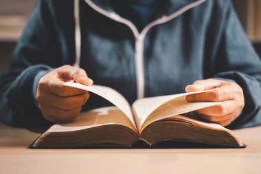 Masada açık bir İncil okuyan bir adam, sığ bir alan derinliği ile sayfaları sıcak kapalı ışık altında çevirmek, Hıristiyan inancını, bağlılığı, çalışmayı ve evdeki sessiz yansımayı sembolize eder..