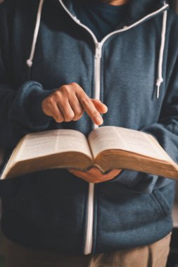 Elinde açık bir İncil tutan ve sayfaları çeviren adam, sıcak kapalı alan ışığı ve sığ alan derinliği, Hıristiyan inancını, bağlılığı, kutsal kitap çalışmasını ve evdeki sessiz ibadeti sembolize ediyor..