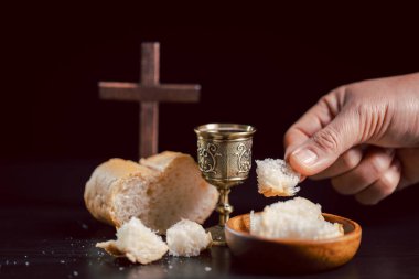 Komünyon sahnesinde, elinde kadehin yanında ekmek ve arka planda ahşap haç, Hıristiyan ayinini, ibadeti, inancı, fedakarlığı ve hatırayı simgeliyor..