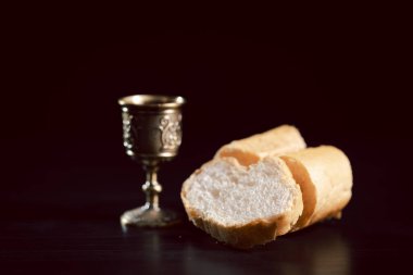 Komünyon, ahşap bir tabakta ekmek, küçük bir bardakta kırmızı şarap ve karanlık bir masanın üzerinde kutsal bir İncil 'in yanında süslü bir kadeh ile kutsanmış, ayini, ibadeti, inancı ve hatırayı simgeliyor..