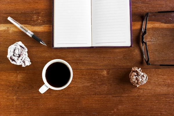 Arbeiten mit leerem Notizbuch auf hölzernem Schreibtischhintergrund mit Kaffeetasse und Altpapier — Stockfoto