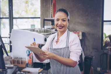  Önlüklü kafe sahibi sipariş verdi. Tezgahın arkasında duran kendine güvenen kadın baristanın portresi. Önlüklü kadın kafe sahibi kameraya bakıyor ve gülümsüyor..