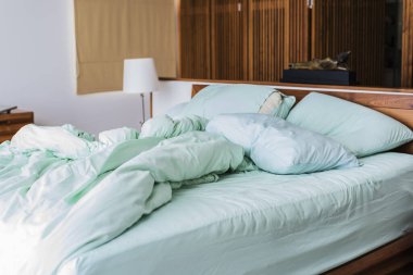 Açık yeşil temalı yatak çarşafları ve yastıkları gece uykusundan sonra dağıtılmış. Dinlenme, iç mekan, konfor ve yatak konsepti.,